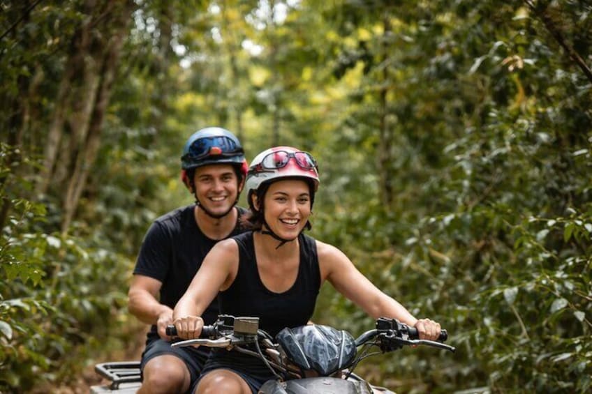 Two people on a motorcycle in a forested area. 1