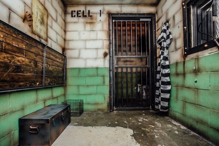 A jail cell with a barred door, a bench, and a striped cloth hanging on the wall. 5