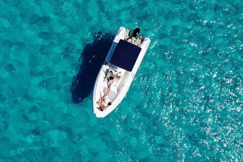 An aerial view of a small white boat with a blue cover on turquoise waters. 1