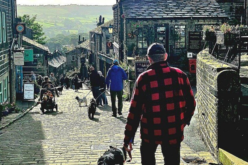 Una calle empedrada en un pueblo, con gente caminando, un perro y edificios con letreros. 5