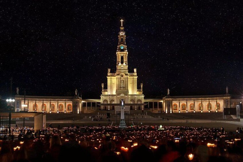 A large illuminated building with a clock tower, surrounded by a crowd of people. 3