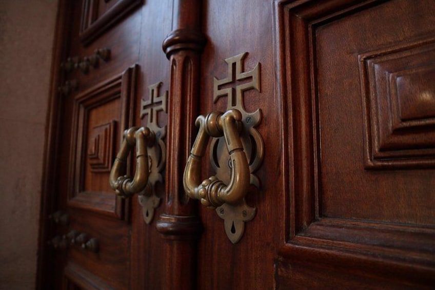 A wooden door with ornate metal knockers and decorative crosses. 5