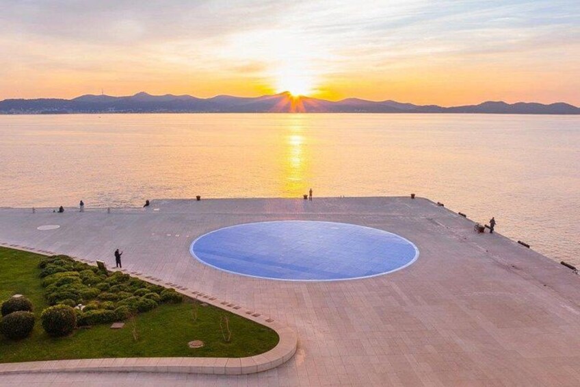 A sunset over a calm body of water with a circular plaza and a grassy area. 4