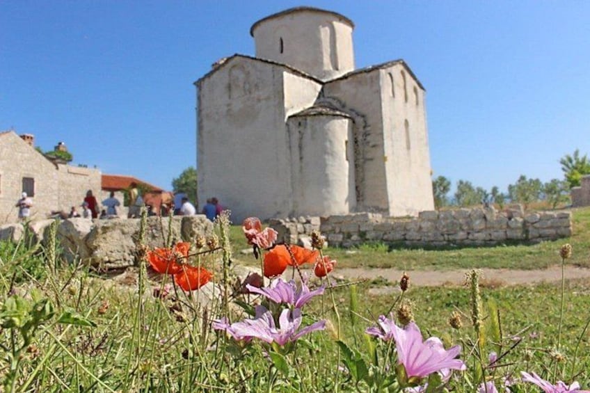 A historical building with a cylindrical tower, surrounded by a grassy field with wildflowers. 2