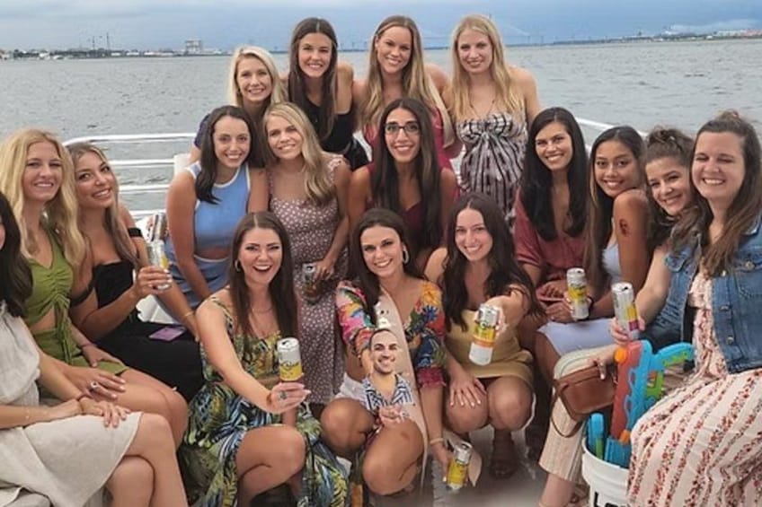 Een groep mensen op een boot met drankjes, een wateroppervlak en een verre kustlijn op de achtergrond. 2