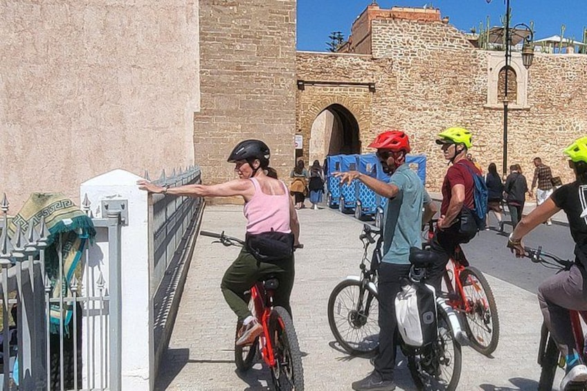 A group of cyclists on a paved path, a stone building, and a metal fence. 3