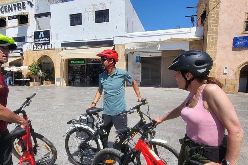 A group of people with bicycles in an urban setting, a hotel, and a building with a sign that reads 'PARFUME.' 2