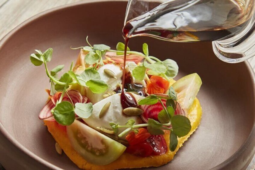 A dish with sliced tomatoes, greens, and a drizzle of sauce in a bowl. 4