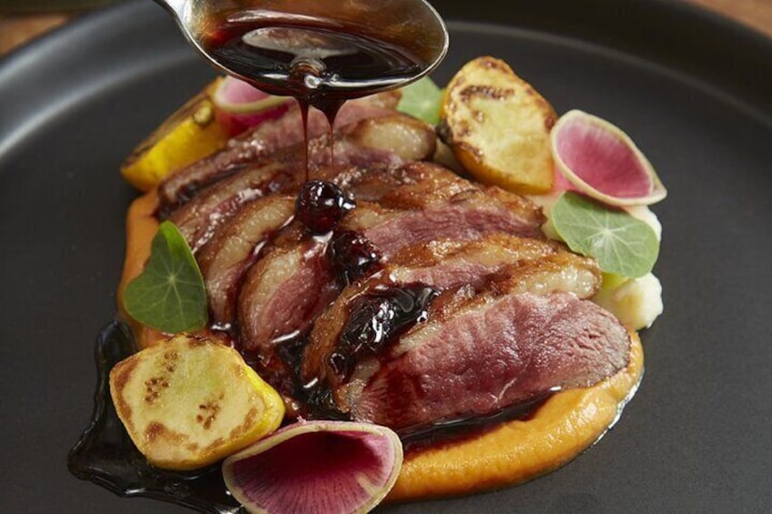 A plate of sliced duck breast with a dark sauce, accompanied by roasted potatoes and citrus slices. 2