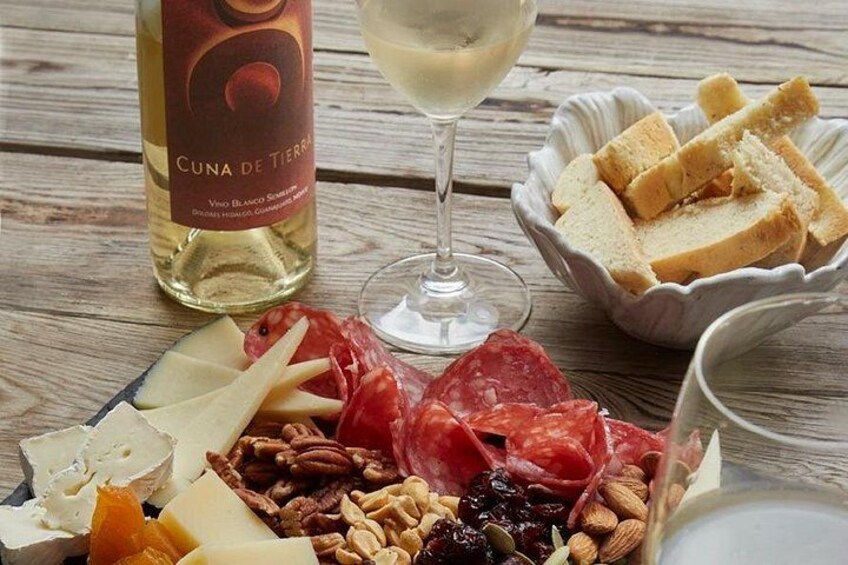 Une planche de charcuterie comprenant divers fromages, viandes, fruits secs et pain, accompagnée d’une bouteille de vin et d’un verre. 1