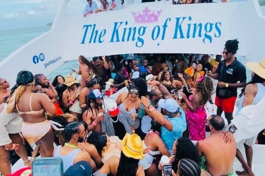 Un bote con gente celebrando, un cartel que dice 'El Rey de Reyes' y un símbolo de corona. 1
