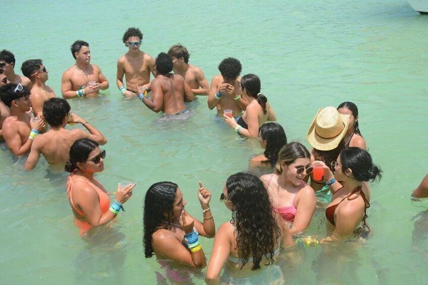 A group of people in a shallow, clear body of water, possibly a beach or pool, with some wearing hats and others holding drinks. 5