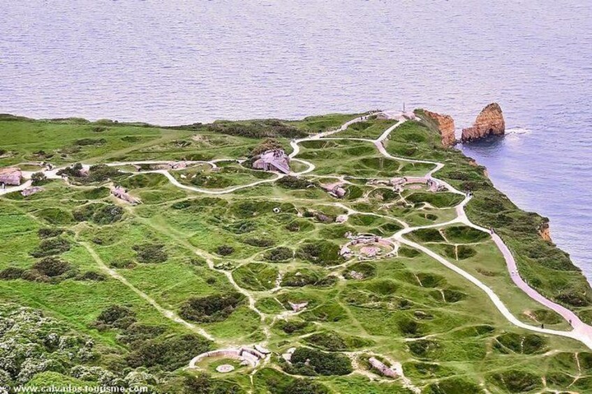 An aerial view of a coastal landscape with green fields, winding paths, and a rocky coastline. 3