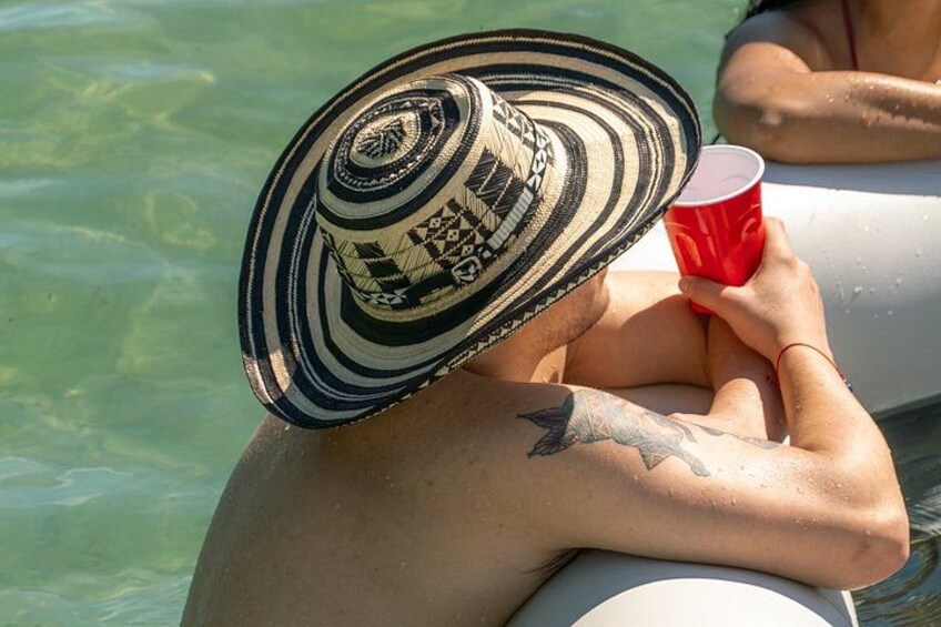 Una persona en una piscina, usando un sombrero estampado y sosteniendo una taza roja. 5