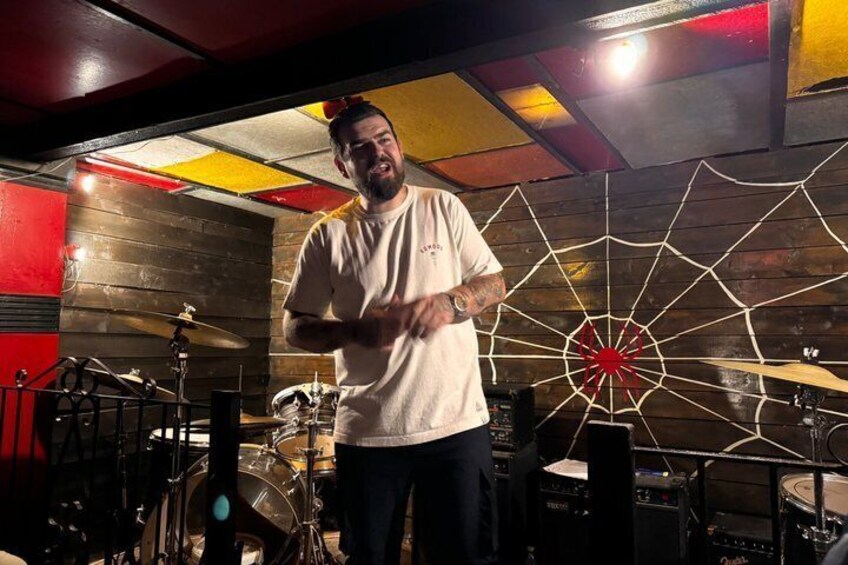 A person standing in a room with a drum set and a large spider web decoration on the wall. 1