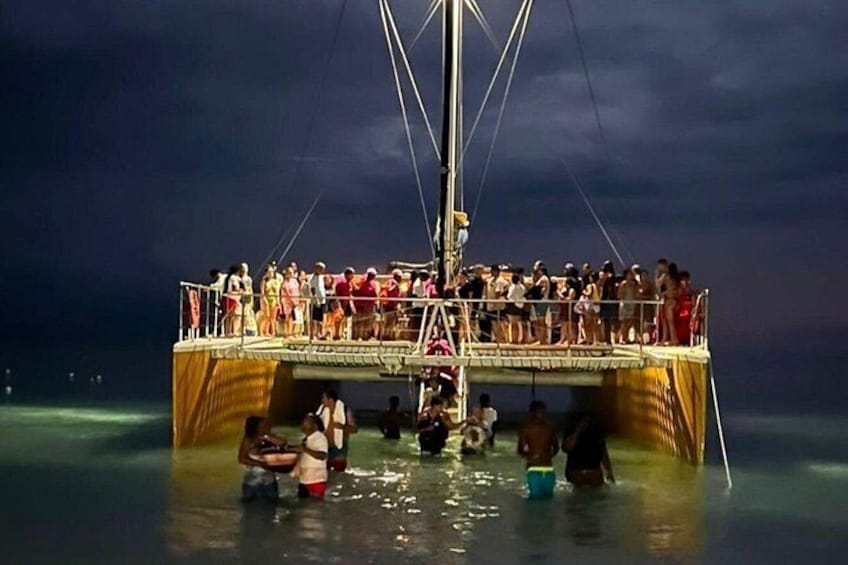 A boat with people on the deck and some in the water. 2