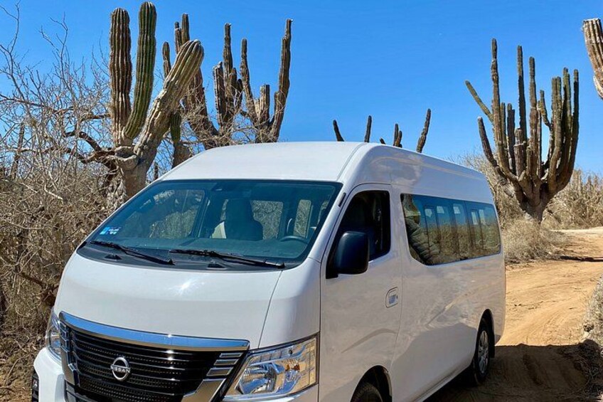 A white van parked on a dirt road with cacti in the background. 2