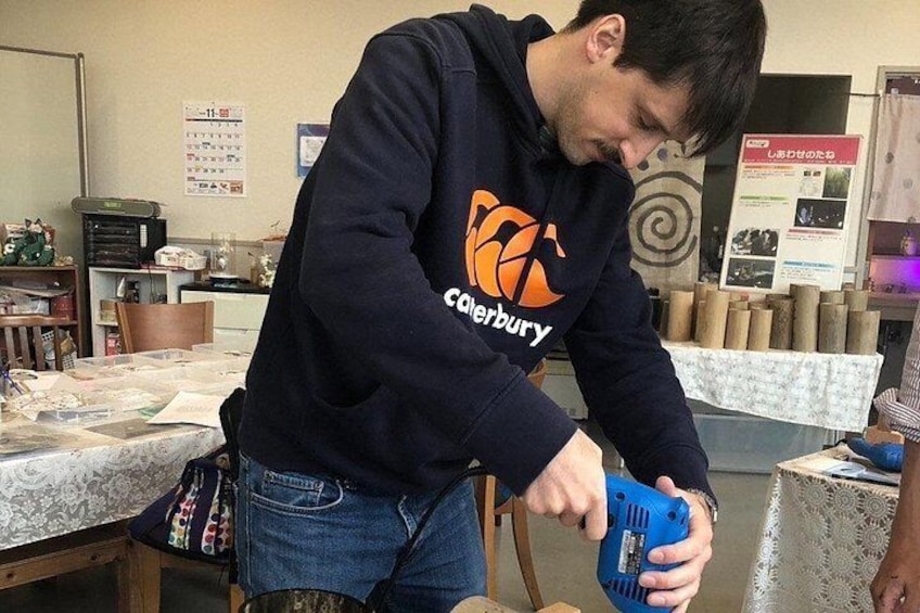 A person wearing a black hoodie with a logo, sitting at a table with papers and a blue device. 4