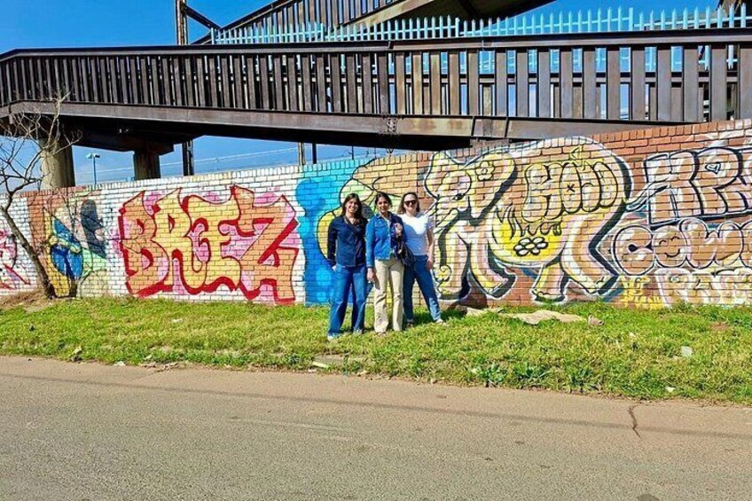 A mural on a brick wall with graffiti, a pedestrian bridge, and a road. 4