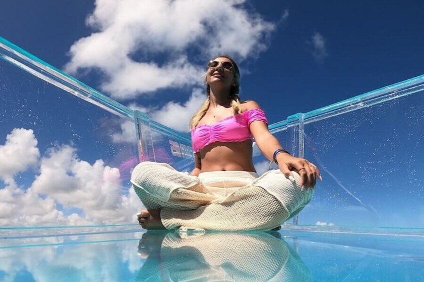 A person sitting on a glass floor with a clear sky and clouds in the background. 4