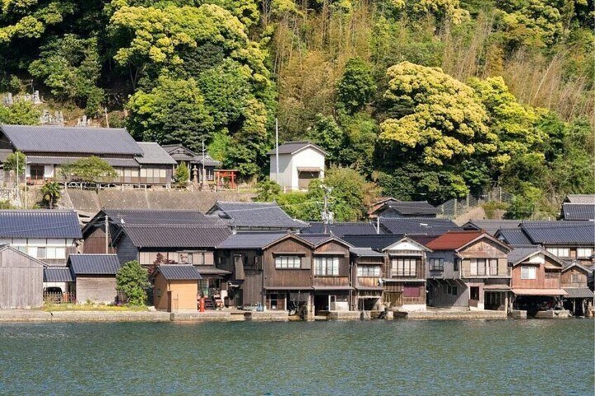 A riverside village with traditional wooden houses and a backdrop of lush green hills. 2