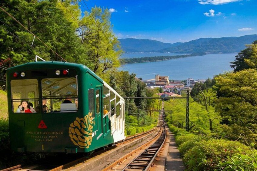 A green cable car on tracks with a scenic view of a lake and mountains. 2