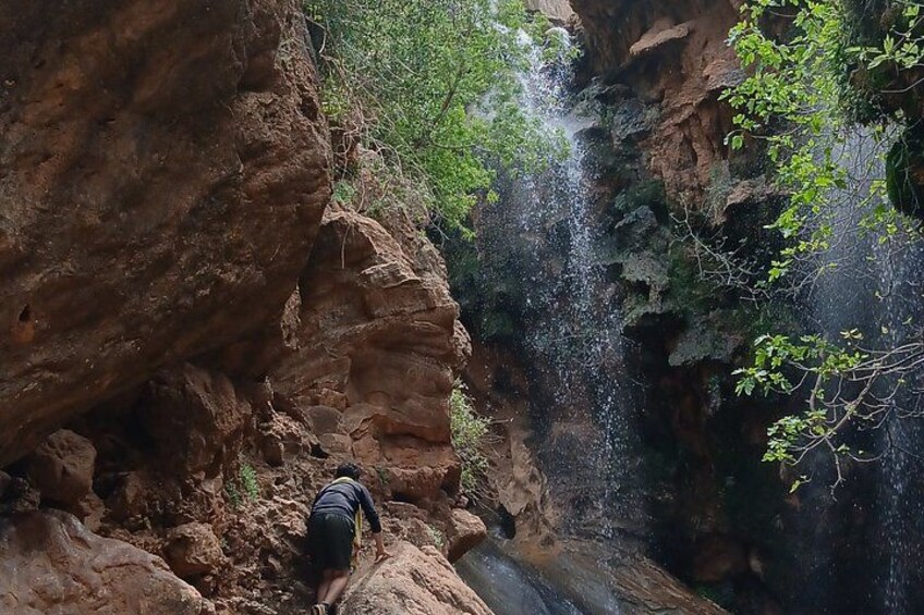 A person climbing a rocky cliff with a waterfall in the background. 2