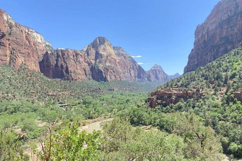 A canyon with red rock cliffs, green vegetation, and a clear blue sky. 2