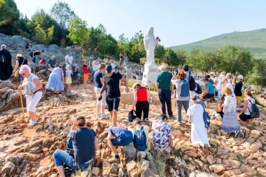 Un groupe de personnes s’est rassemblé autour d’une statue blanche, sur un terrain rocheux, avec des arbres et des collines en arrière-plan. 5