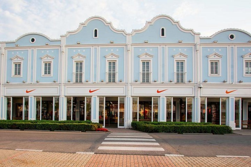 A row of light blue buildings with white trim and arched windows, featuring Nike logos on the ground floor. 3