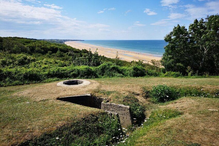 Ett kustlandskap med en strand, tät vegetation och en av människan skapad konstruktion. 2