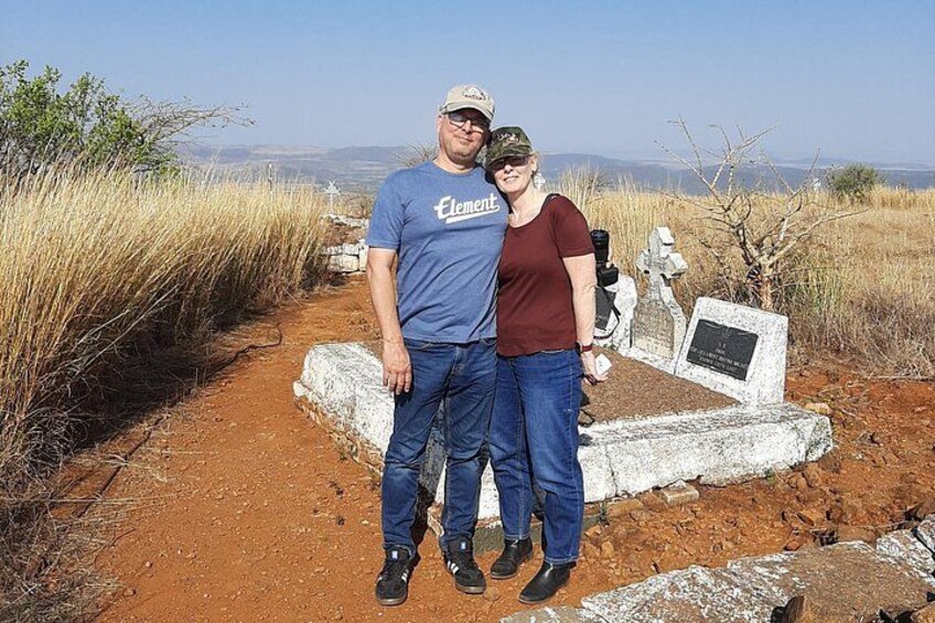 A man and a woman standing on a dirt path with a cemetery in the background. 4