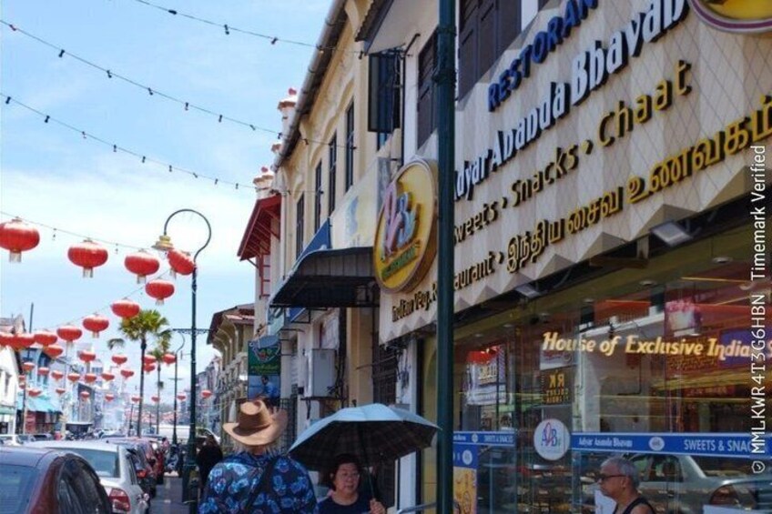 Calle con faroles rojos, una tienda de comida y un letrero que dice 'House of Exclusive Indian Sweets & Snacks'. 4