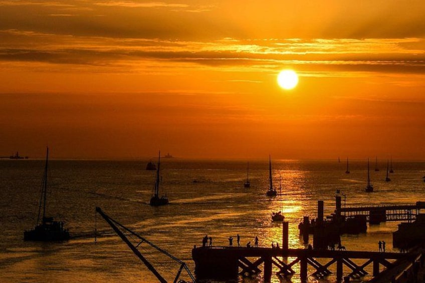 A sunset over a body of water with sailboats and a pier. 4