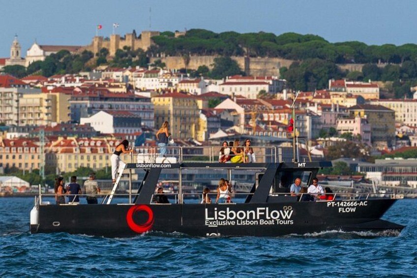 A boat with 'LisbonFlow' written on it, sailing on water with a cityscape in the background. 2