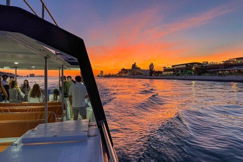 A sunset view from a boat with people on deck, a city skyline in the background, and calm water. 4