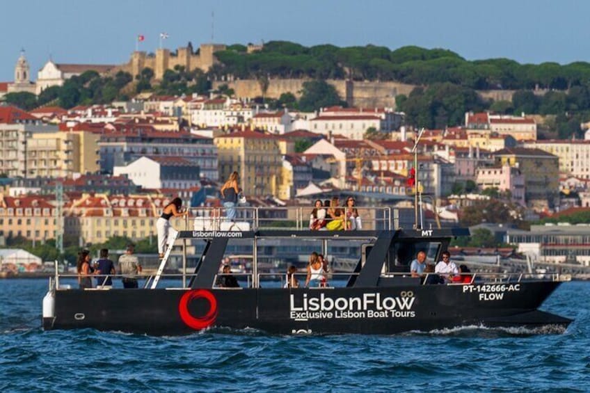 A boat named 'LisbonFlow' with passengers, sailing near a city with historical buildings. 1