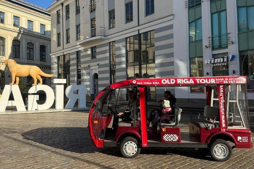 A red tour bus with 'Old Riga Tour' written on it, parked in front of a building with large letters spelling 'RIGA'. 5