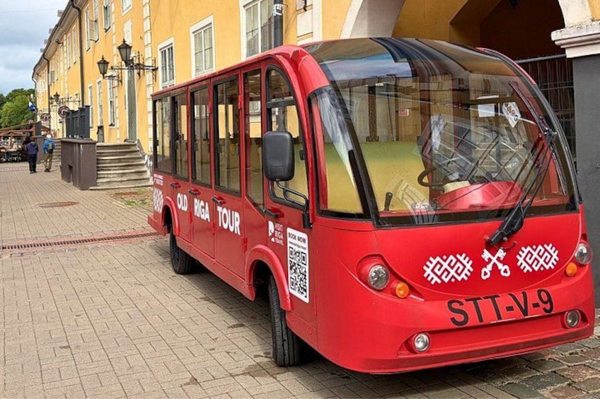 A red tour bus parked on a brick pavement with a building in the background. 1