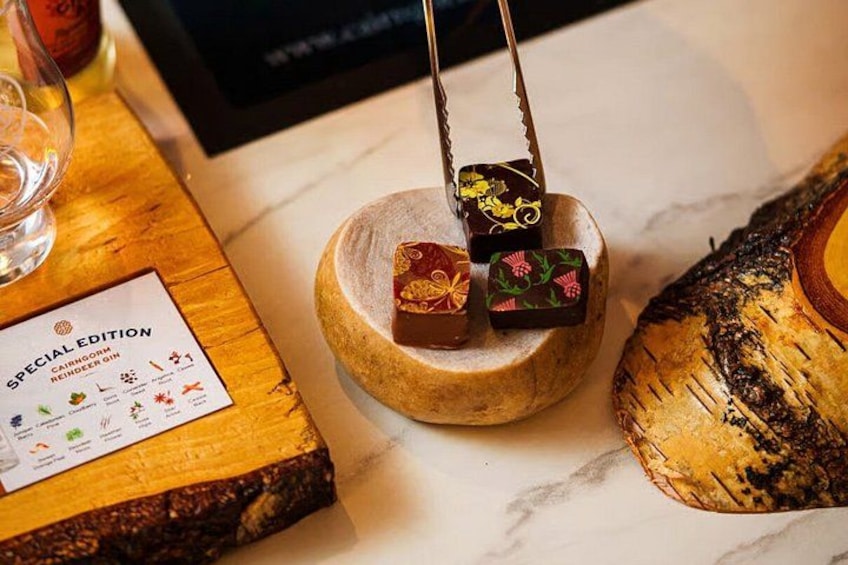 A wooden board with three pieces of chocolate on it, a bottle of gin, and a menu. 2