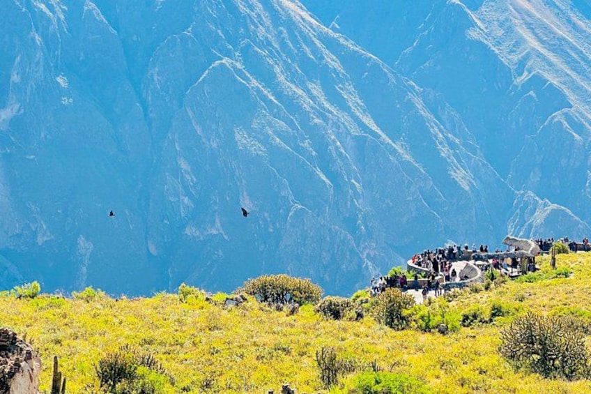 A mountainous landscape with a group of people gathered around a circular structure, possibly a viewing platform, overlooking the valley. 1