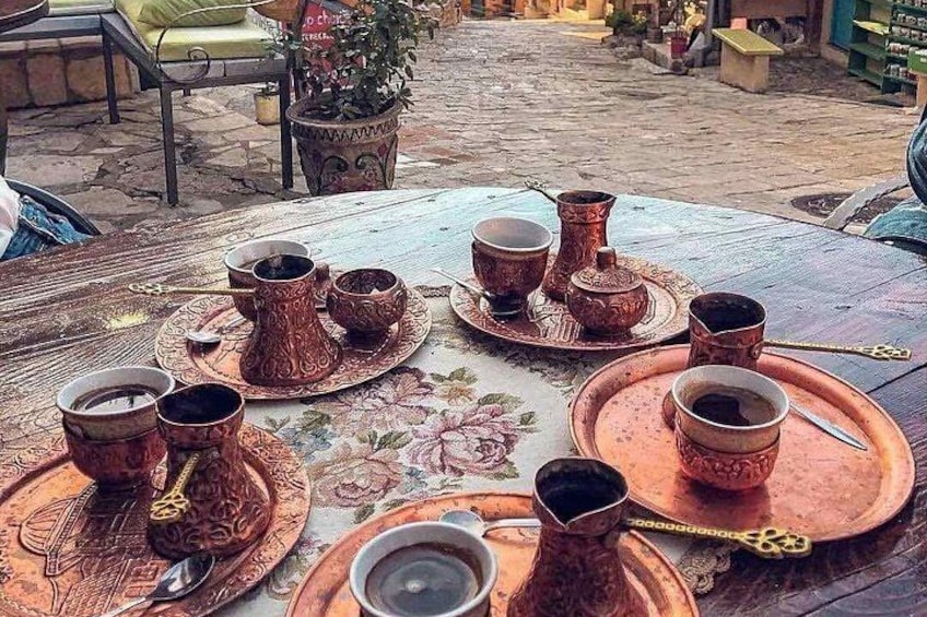 A traditional tea set on a table outdoors with a floral tablecloth. 2