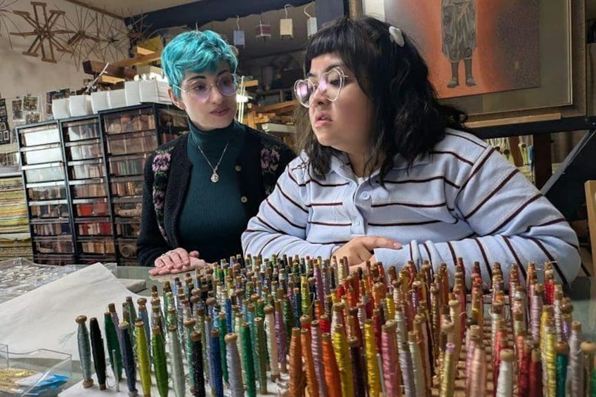Two individuals seated at a table with a variety of colorful spools of thread. 1