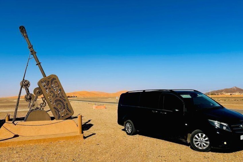 A black SUV parked on a desert road with a mounted weapon system beside it. 4