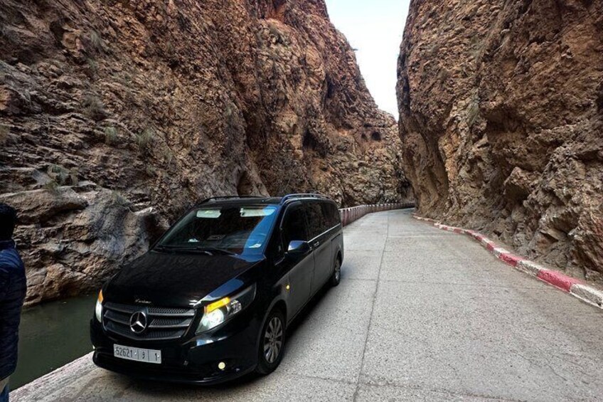 A black car parked on a paved road between rocky cliffs. 2