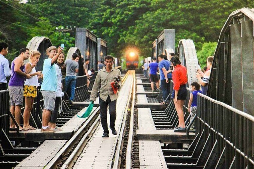 A bridge with people walking and standing, a train in the background, and greenery around. 2