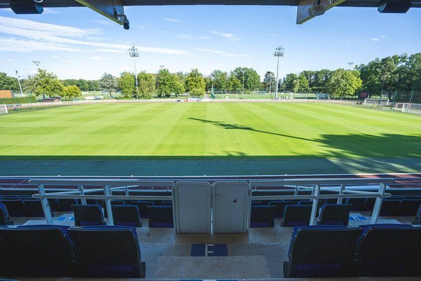 A baseball field with green grass, empty spectator seats, and trees in the background. 2