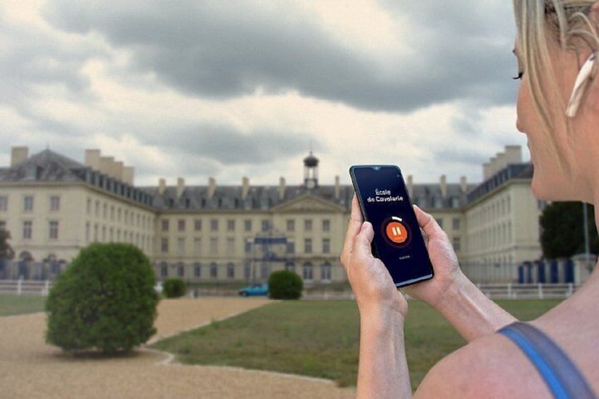A person holding a smartphone with an app interface, standing in front of a large historic building with a dome. 3