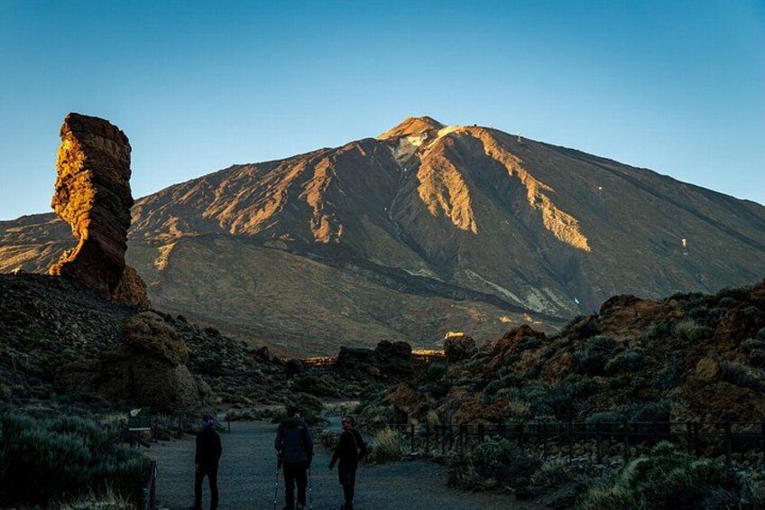 A mountain landscape with a prominent rock formation and hikers in the foreground. 3