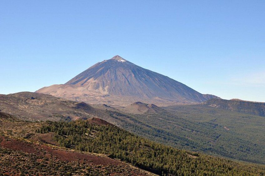 A mountain with a snow-capped peak, forested slopes, and a clear sky. 1